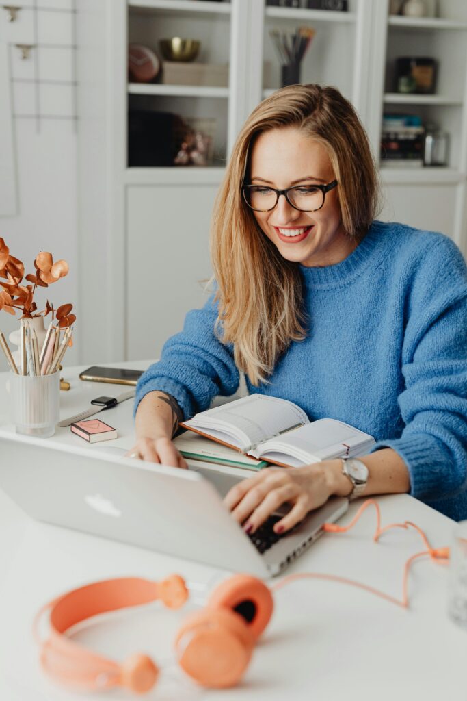 pexels-photo-5908728-5908728 A cheerful woman in a blue sweater working remotely with a laptop in a cozy home setting.